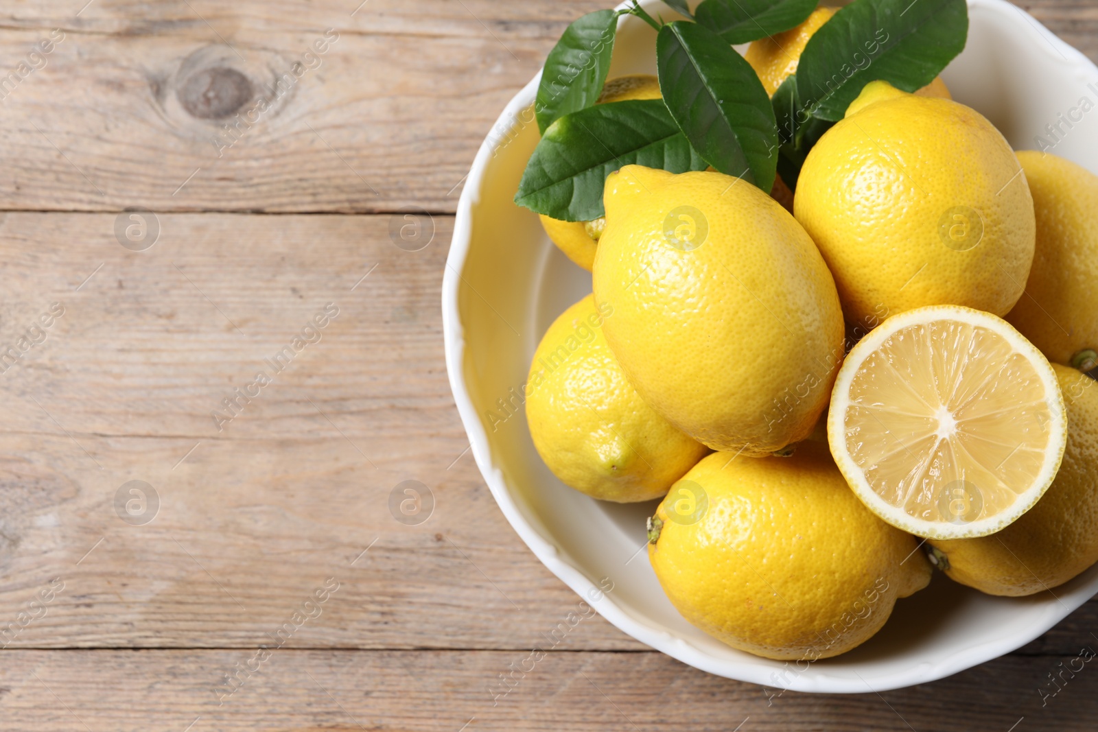 Photo of Fresh lemons and green leaves on wooden table, top view. Space for text