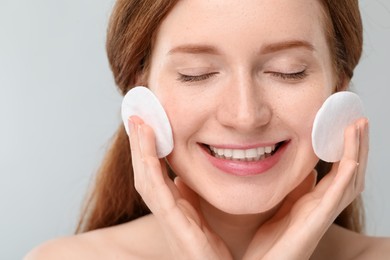 Photo of Smiling woman with freckles wiping face on grey background, closeup