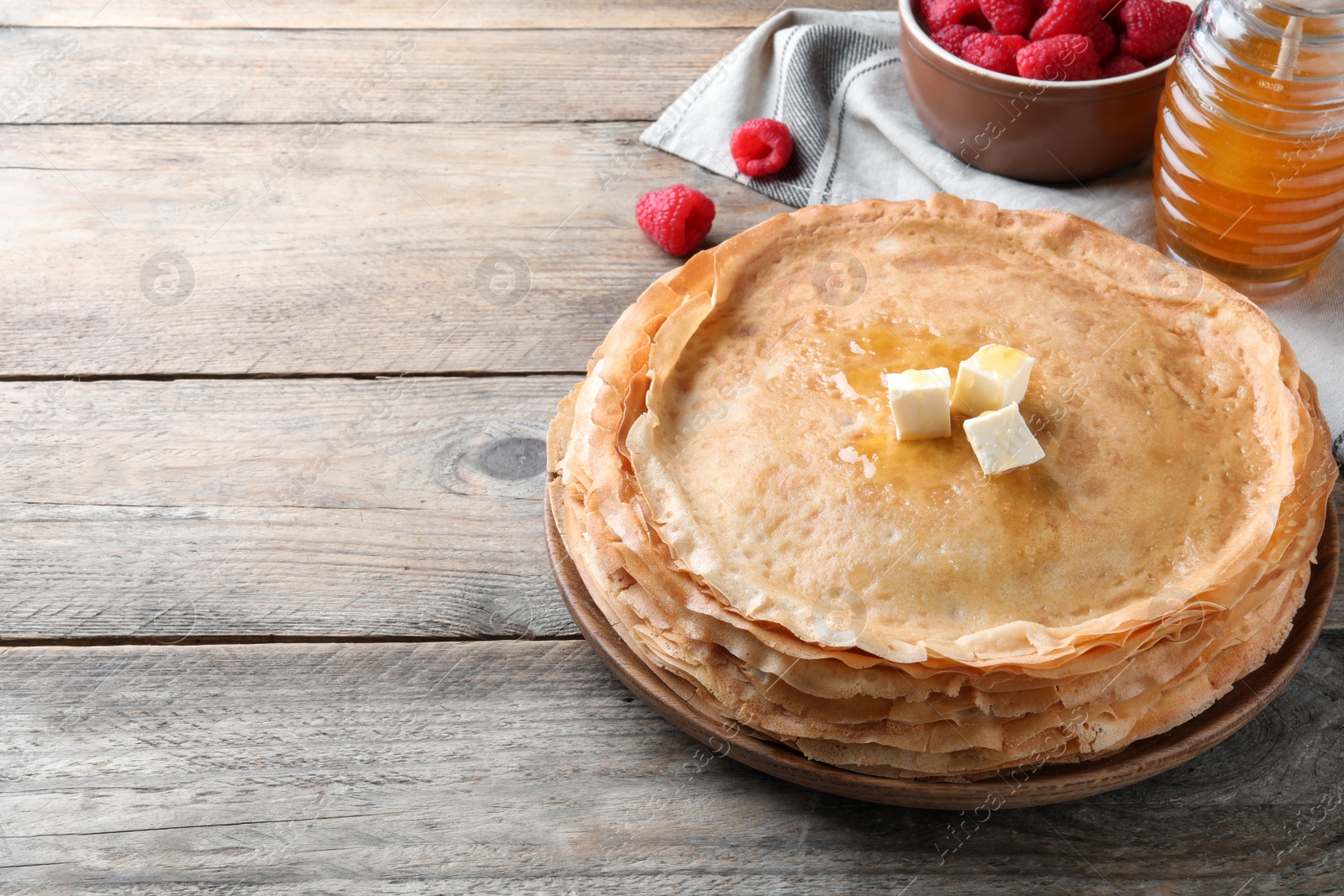 Photo of Stack of delicious crepes served with butter, honey and raspberries on wooden table. Space for text