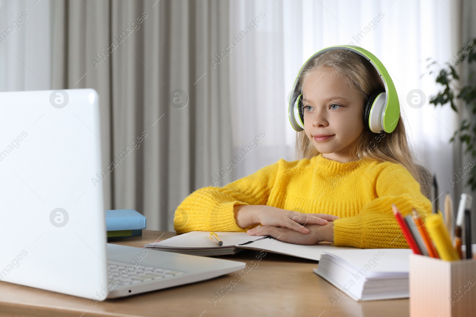 Photo of Cute little girl with modern laptop studying online at home. E-learning