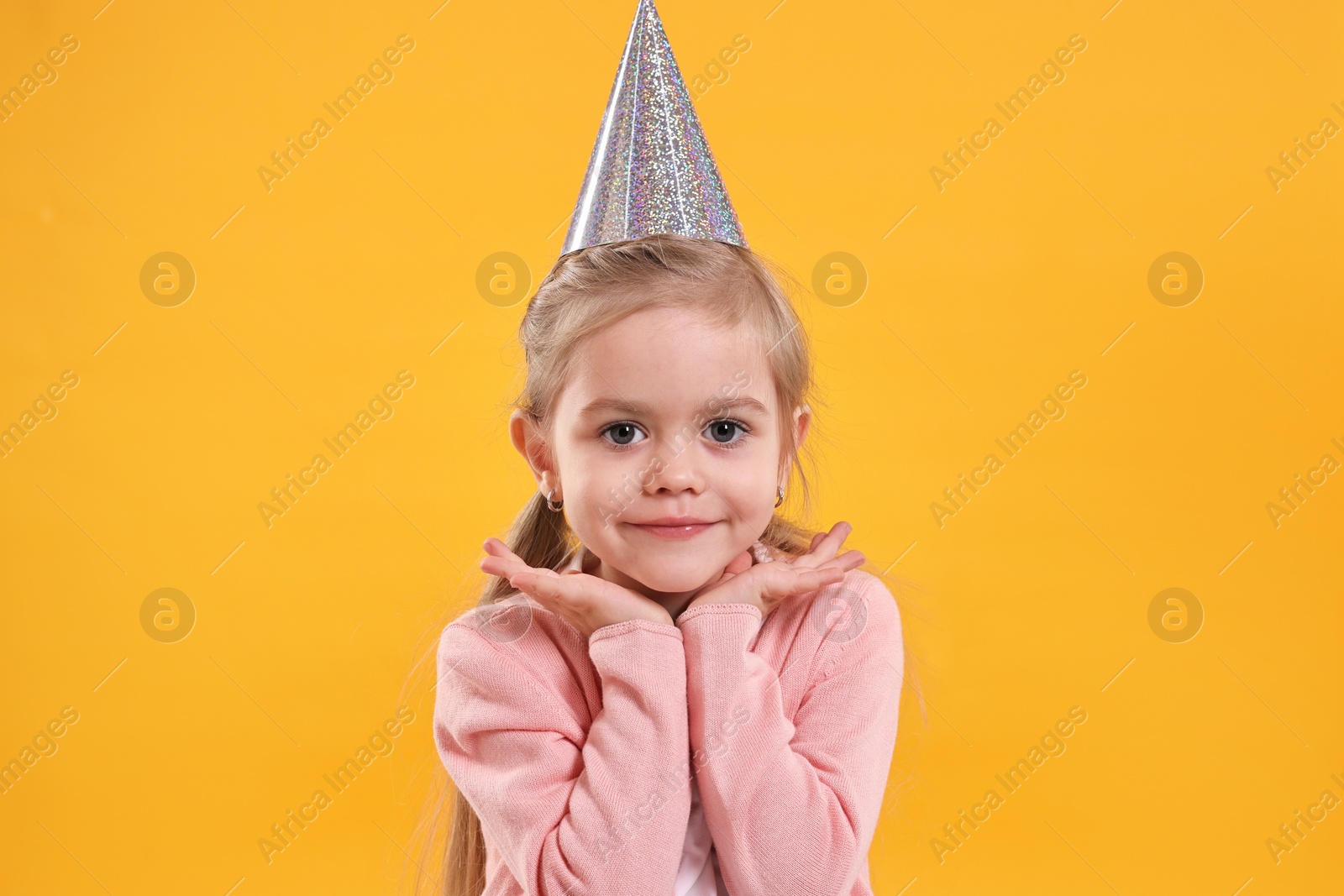 Photo of Birthday celebration. Cute little girl in party hat on orange background