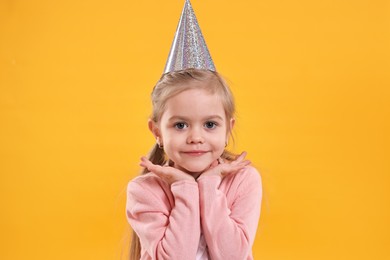 Photo of Birthday celebration. Cute little girl in party hat on orange background