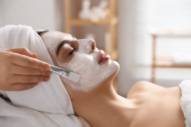Cosmetologist applying mask on woman's face in spa salon, closeup