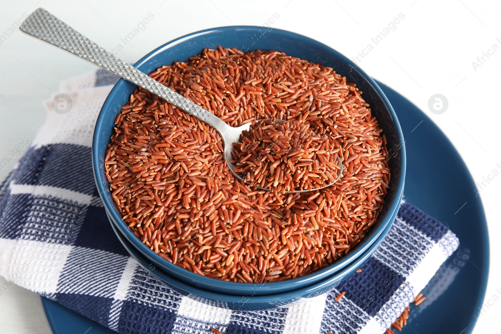 Photo of Bowl with uncooked red rice and spoon on white table