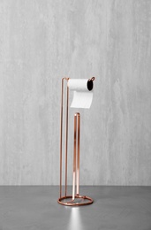 Holder with toilet paper roll near gray wall