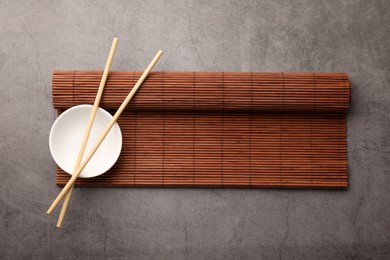 Photo of Rolled bamboo mat, chopsticks and bowl on grey table, top view