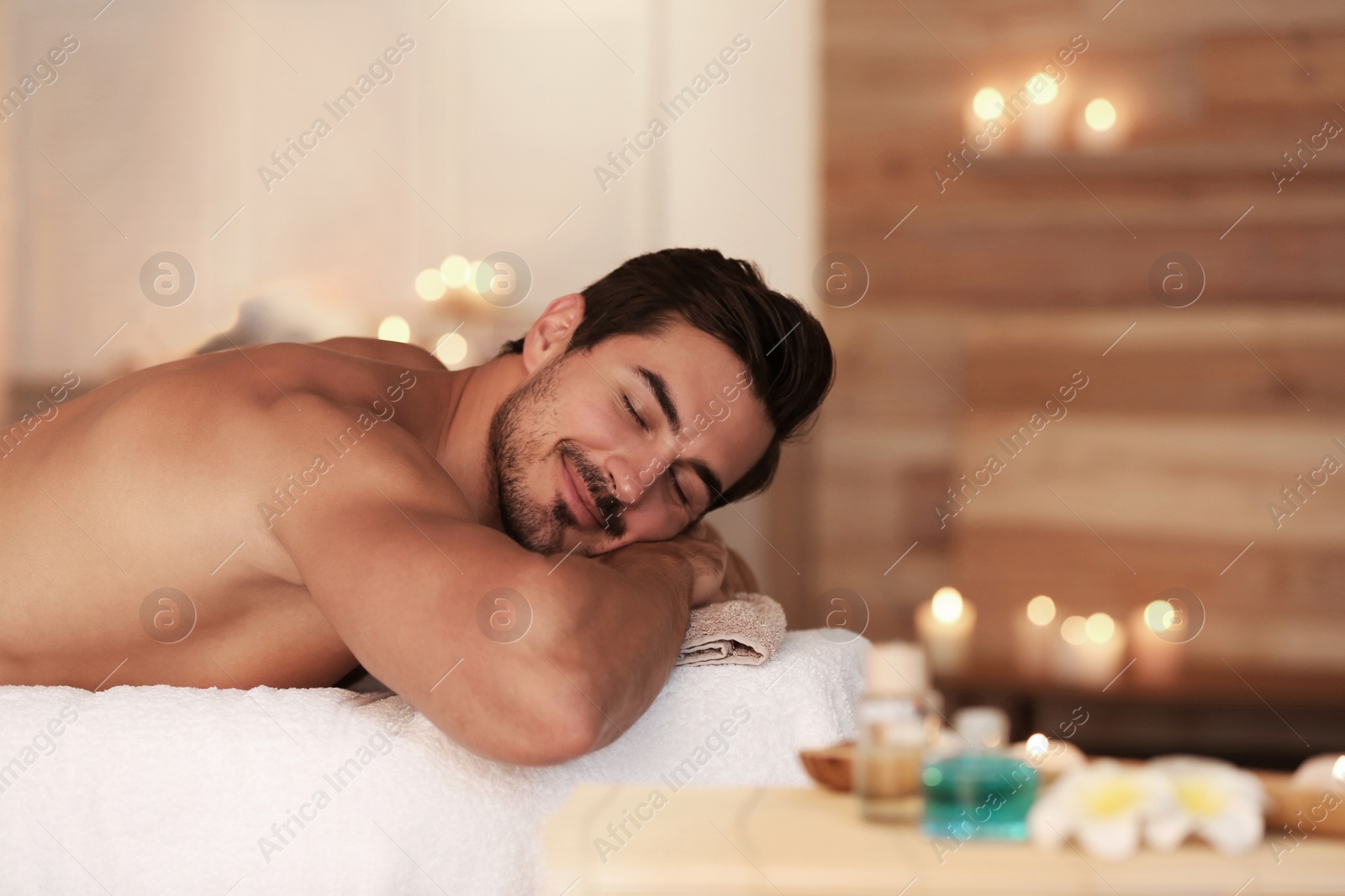 Photo of Handsome young man relaxing on massage table in spa salon, space for text