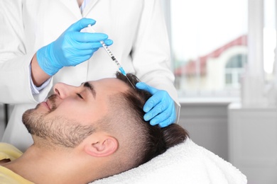 Photo of Young man with hair loss problem receiving injection in salon