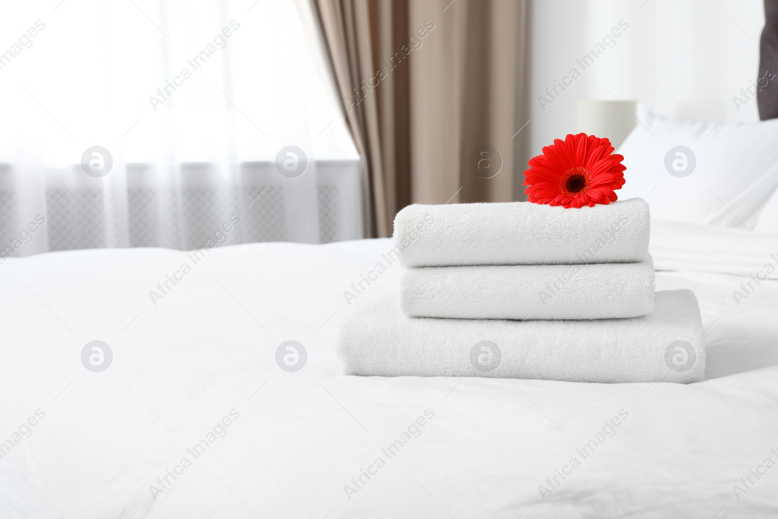 Photo of Stack of fresh towels with flower on bed indoors. Space for text