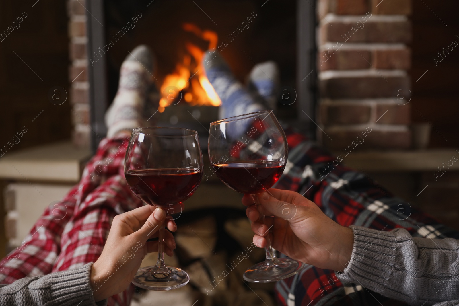 Photo of Couple with glasses of red wine near burning fireplace, closeup