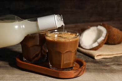 Pouring coconut syrup into glass with tasty coffee at wooden table, closeup