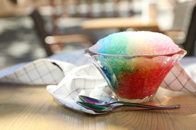 Photo of Rainbow shaving ice in glass dessert bowl and spoons on wooden table outdoors, closeup