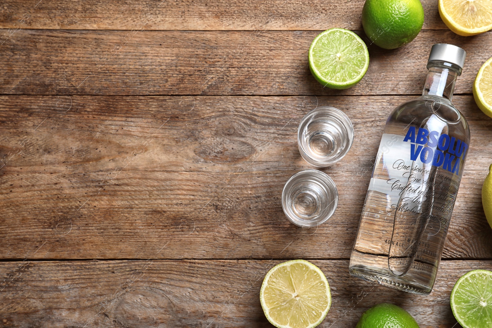 Photo of MYKOLAIV, UKRAINE - OCTOBER 04, 2019: Absolut vodka, citrus fruits and shot glasses on wooden table, flat lay. Space for text