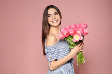 Portrait of beautiful smiling girl with spring tulips on pink background. International Women's Day