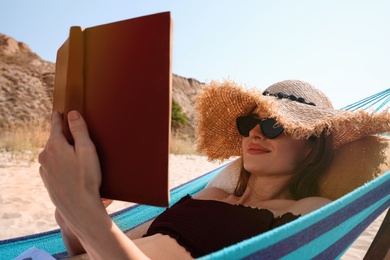 Photo of Young woman reading book in hammock on beach