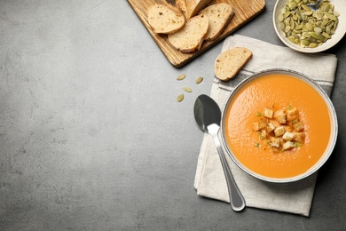 Photo of Tasty creamy pumpkin soup served with bread and seeds on grey table, flat lay. Space for text