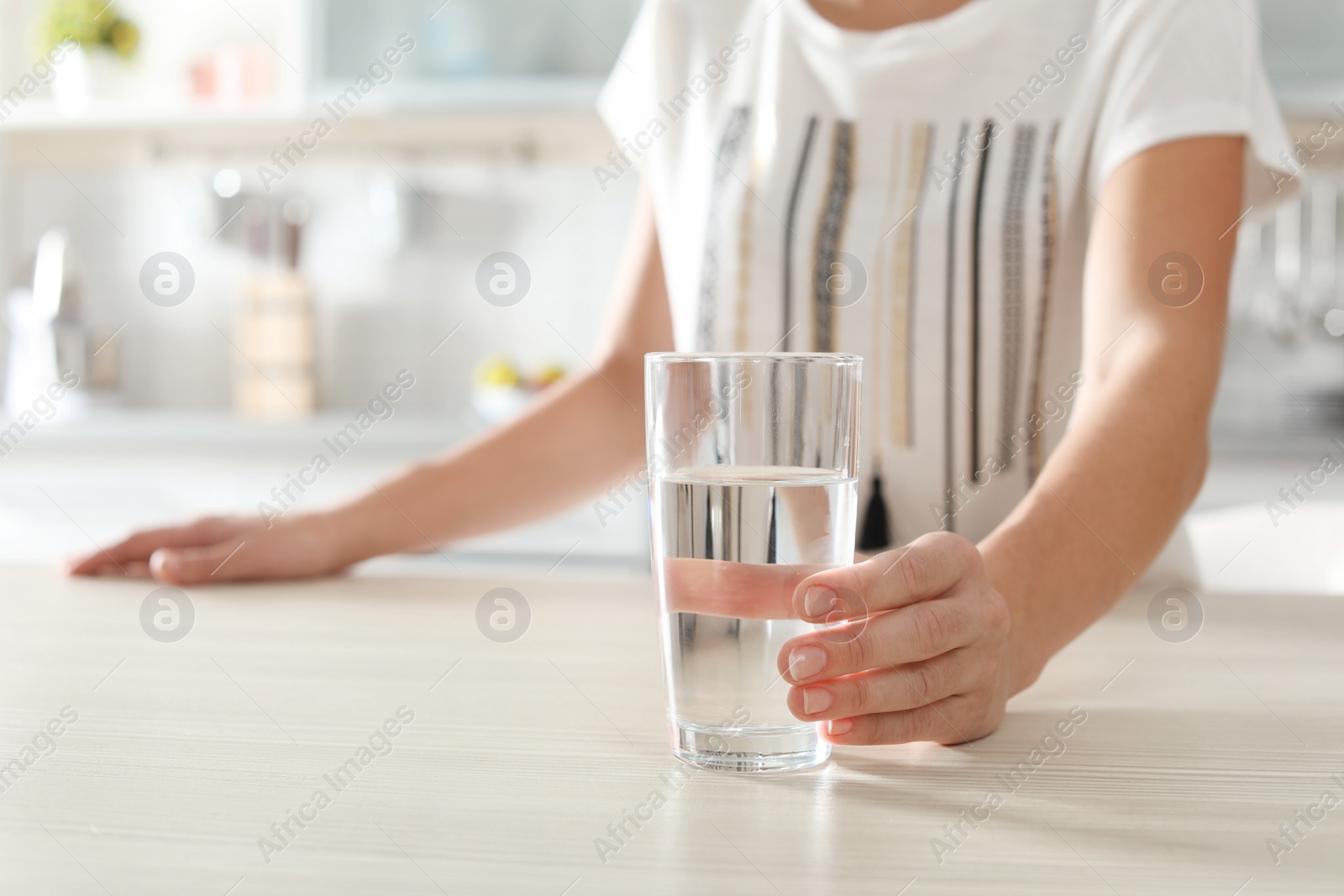 Photo of Woman holding glass with clean water on table in kitchen, closeup