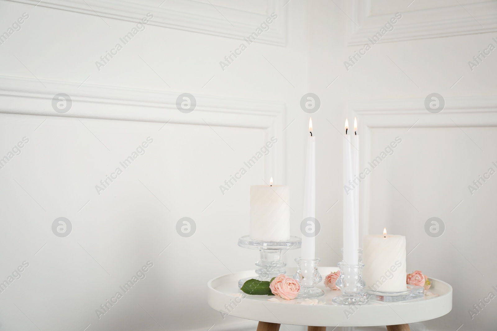 Photo of Elegant candlesticks with burning candles and flowers on white table. Space for text