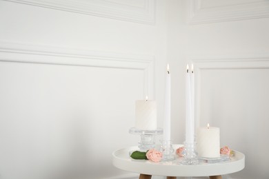 Elegant candlesticks with burning candles and flowers on white table. Space for text