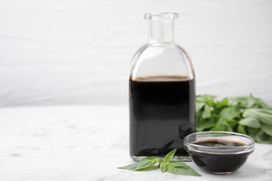 Organic balsamic vinegar and basil on white marble table, space for text