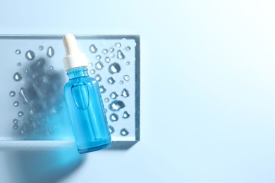 Bottle of cosmetic serum on light blue background, top view. Space for text