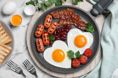 Photo of Delicious breakfast with heart shaped fried eggs and  sausages served on white marble table, flat lay