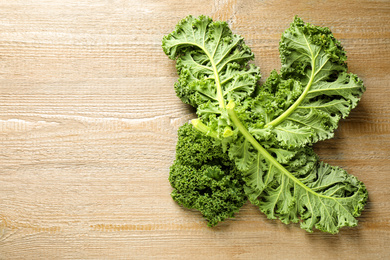 Photo of Fresh kale leaves on wooden table, top view. Space for text