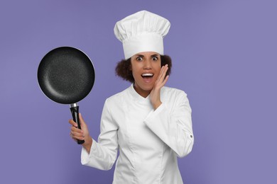 Photo of Emotional female chef in uniform holding frying pan on purple background