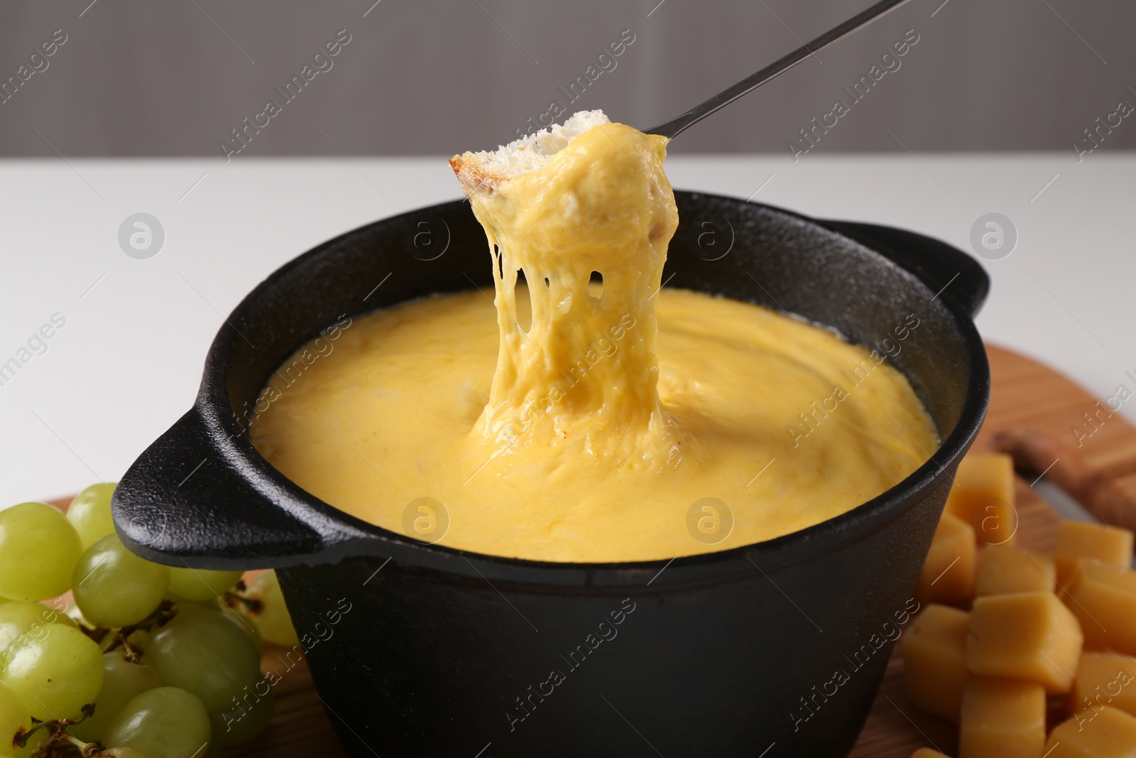 Photo of Dipping piece of bread into fondue pot with tasty melted cheese at table, closeup