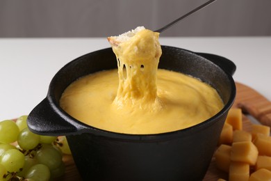 Photo of Dipping piece of bread into fondue pot with tasty melted cheese at table, closeup