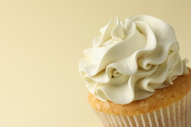 Photo of Tasty vanilla cupcake with cream on pale yellow background, closeup. Space for text