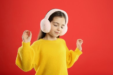 Photo of Cute girl wearing stylish earmuffs on red background