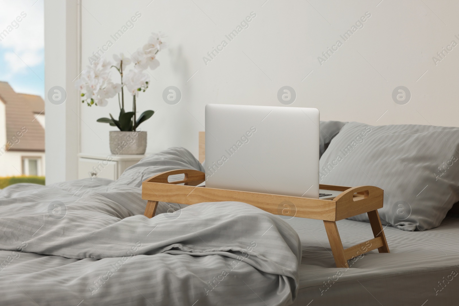 Photo of Wooden tray table with laptop and smartphone on bed indoors