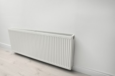 Photo of Modern radiator on white wall indoors. Central heating system