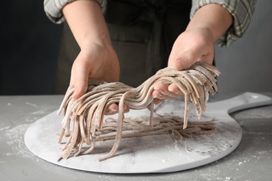 Photo of Woman making soba (buckwheat noodles) at grey table, closeup