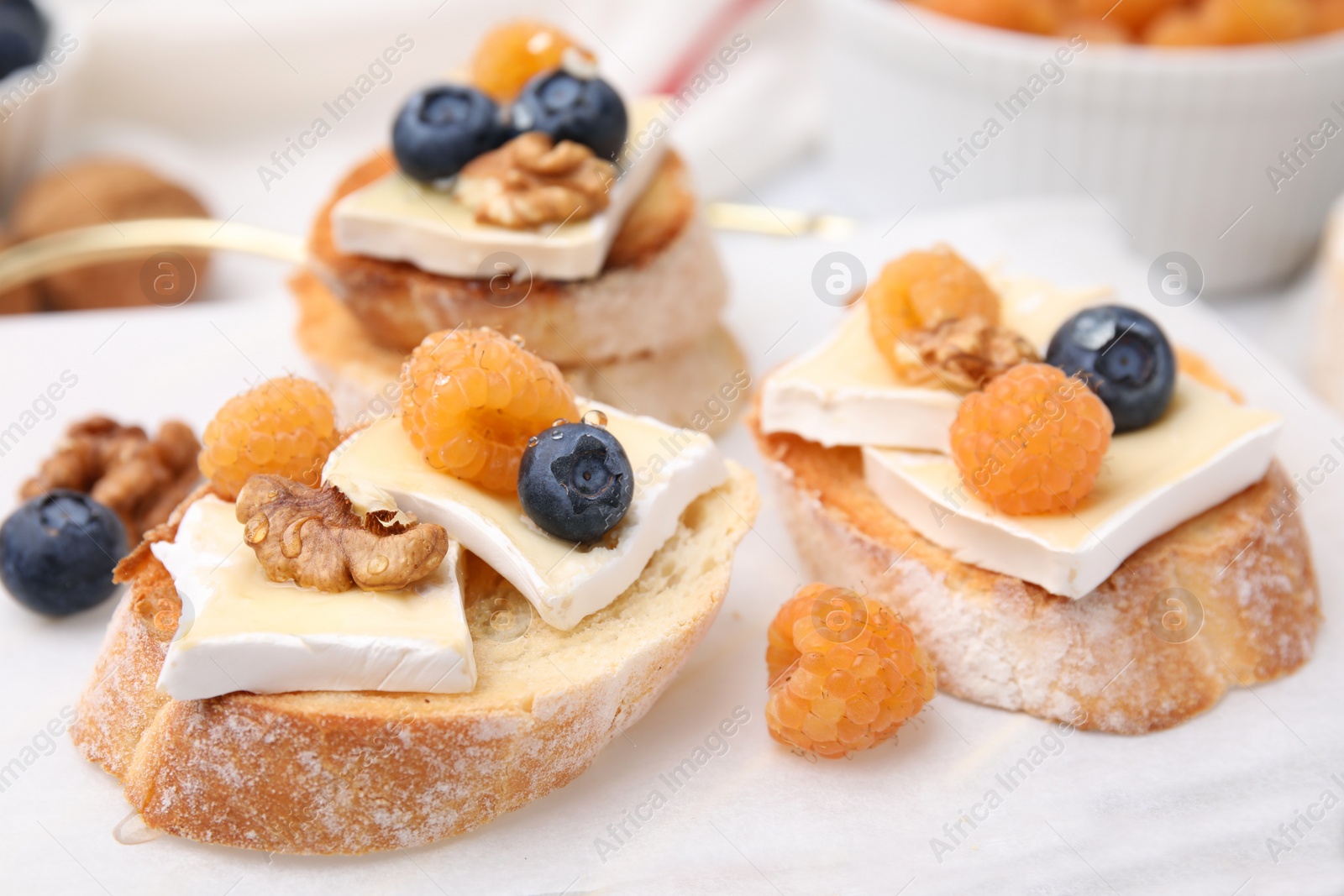 Photo of Tasty sandwiches with brie cheese, fresh berries and walnuts on white table, closeup