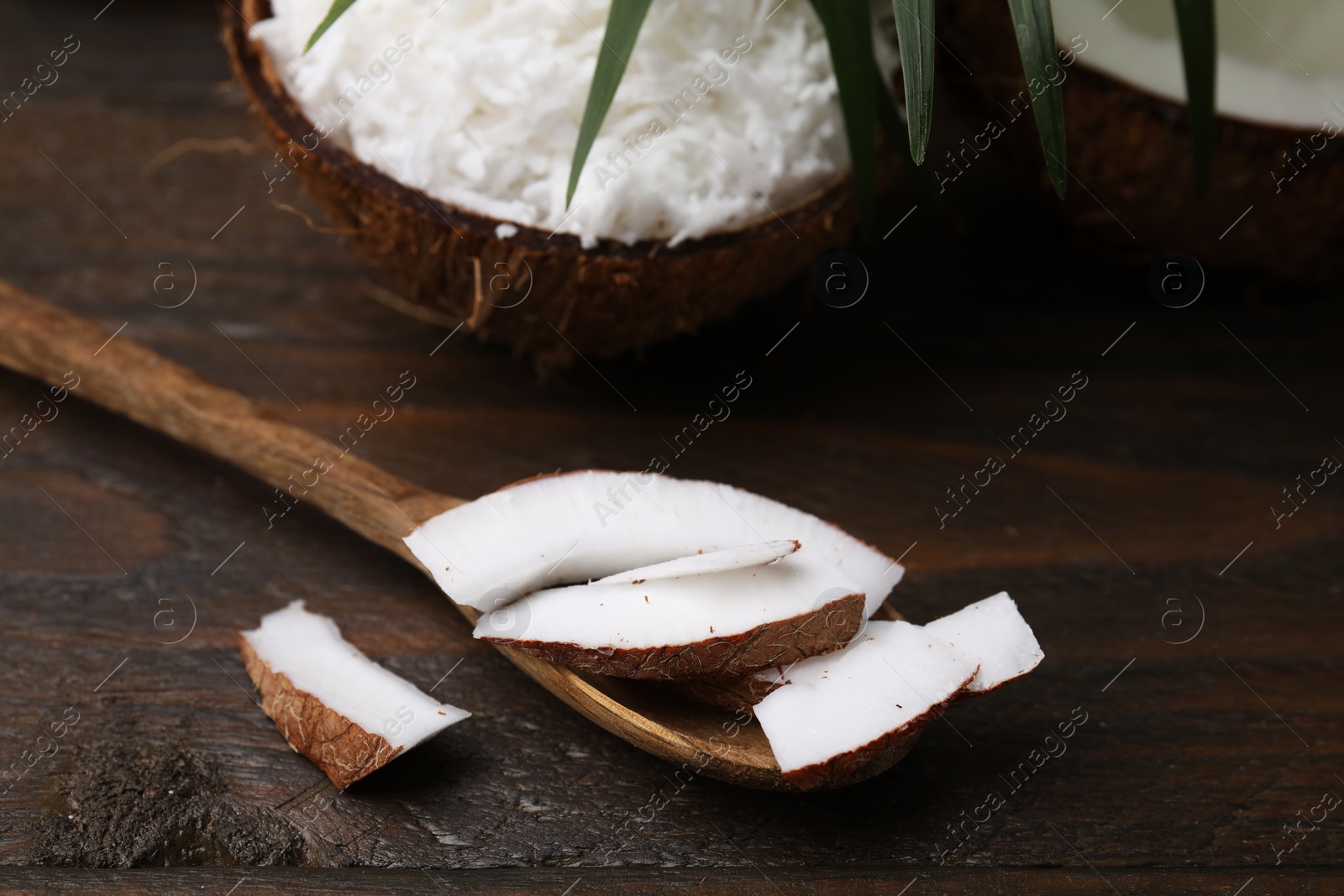 Photo of Coconut pieces, spoon and nut on wooden table, closeup