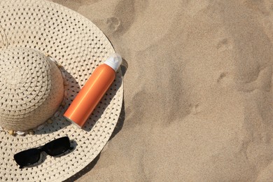 Sunscreen, hat and sunglasses on sand, top view with space for text. Sun protection care