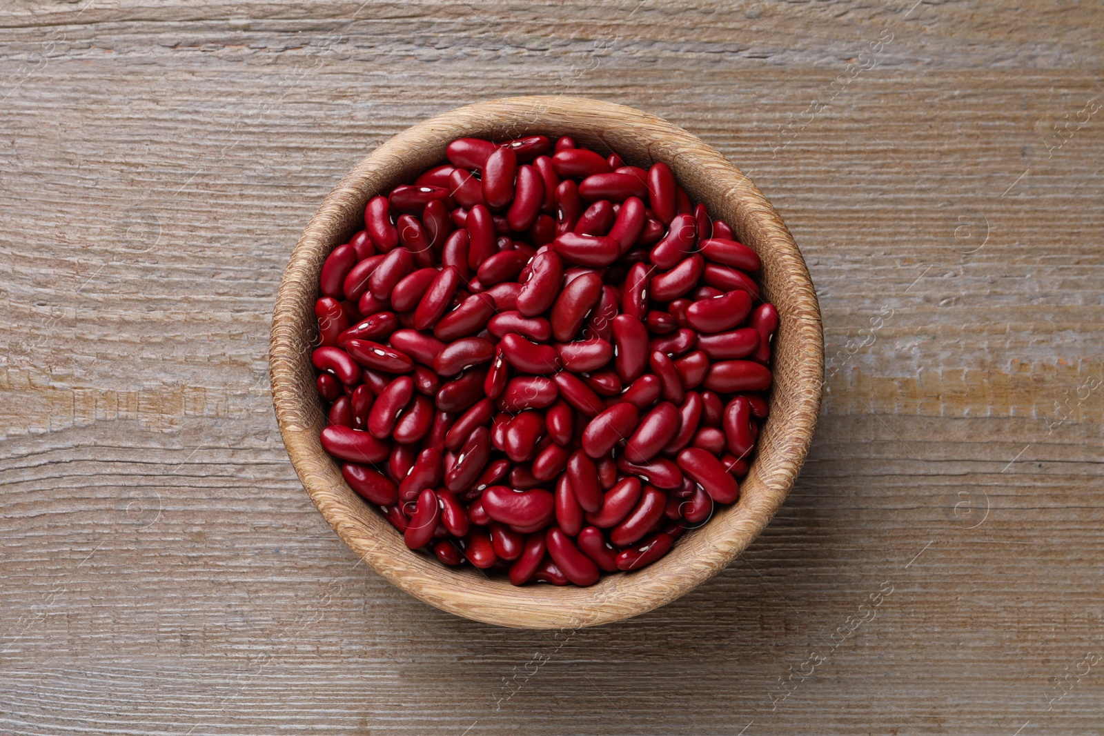 Photo of Raw red kidney beans in bowl on wooden table, top view