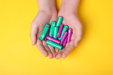 Photo of Woman holding many different batteries on yellow background, top view
