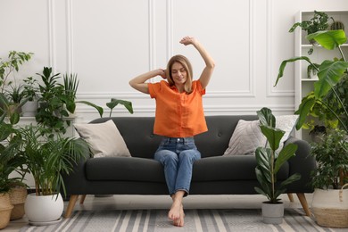 Woman stretching on sofa surrounded by beautiful potted houseplants at home