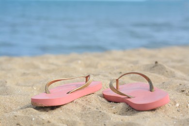 Photo of Stylish flip flops on sandy beach near sea