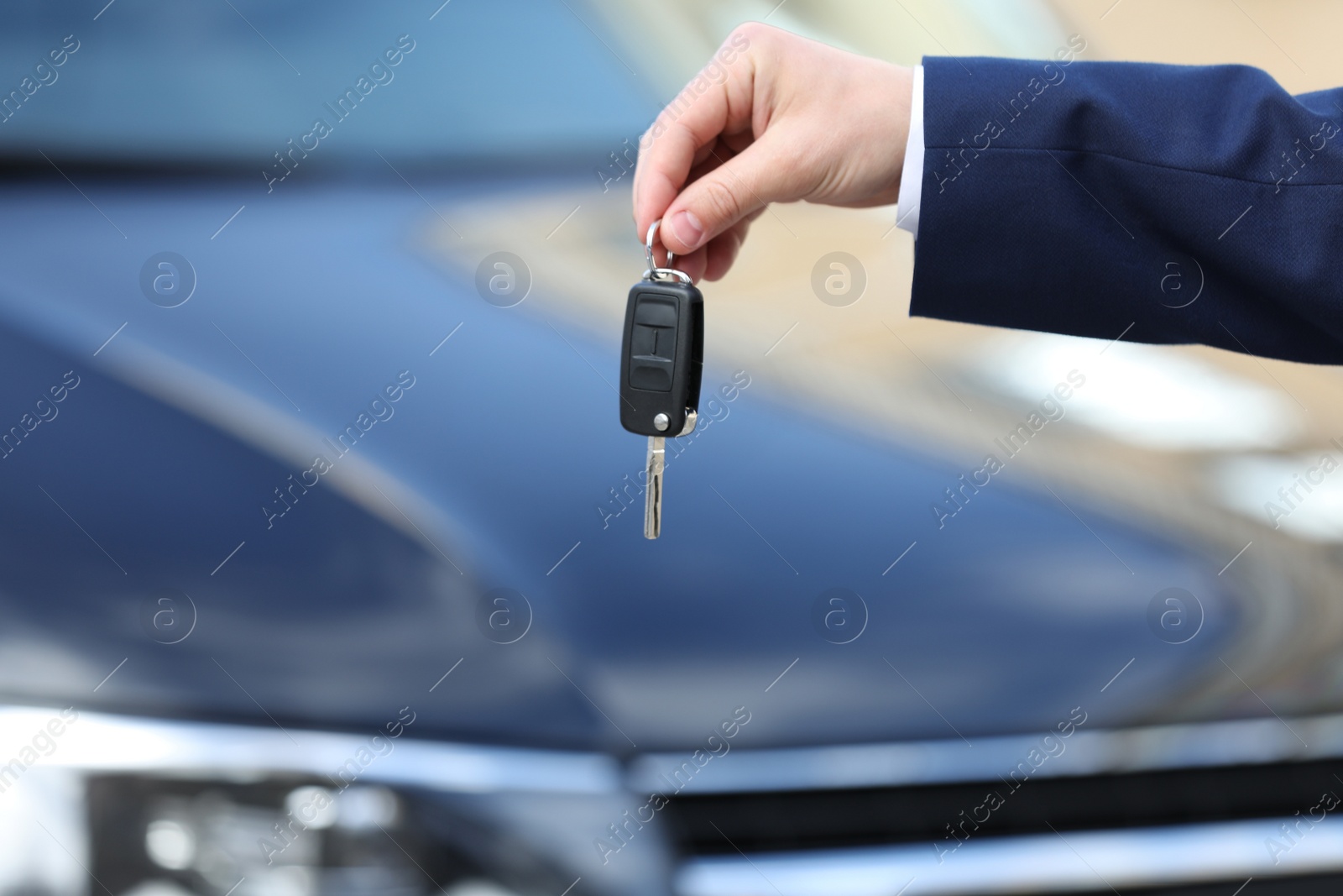 Photo of Man holding key in modern auto dealership, closeup. Buying new car