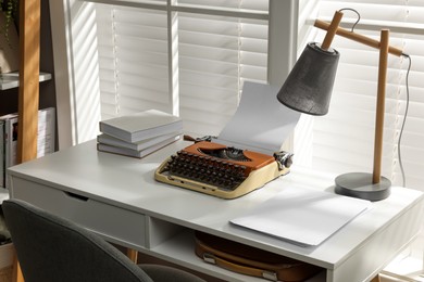 Photo of Comfortable writer's workplace with typewriter on desk in front of window