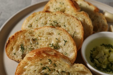 Tasty baguette with garlic, oil and dill in plate, closeup