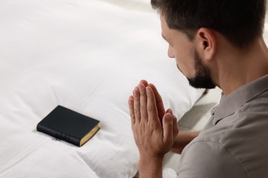 Religious man with Bible praying in bedroom, closeup