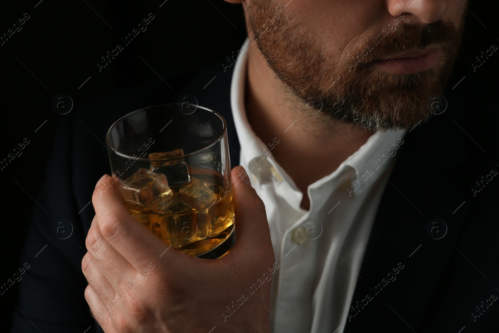 Photo of Man holding glass of whiskey with ice cubes on black background, closeup