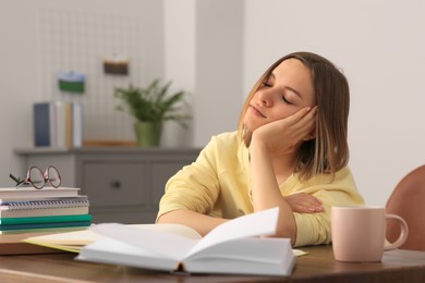 Young tired woman studying at wooden table in room