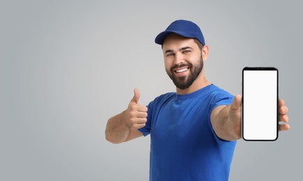 Image of Happy courier holding smartphone with empty screen and showing thumbs up on grey background. Banner design with space for text