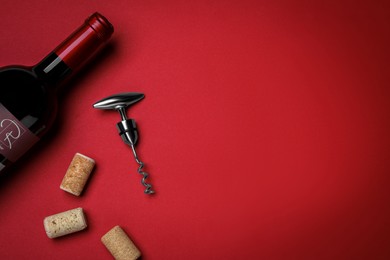 Photo of Corkscrew with wine bottle and stoppers on red background, flat lay. Space for text